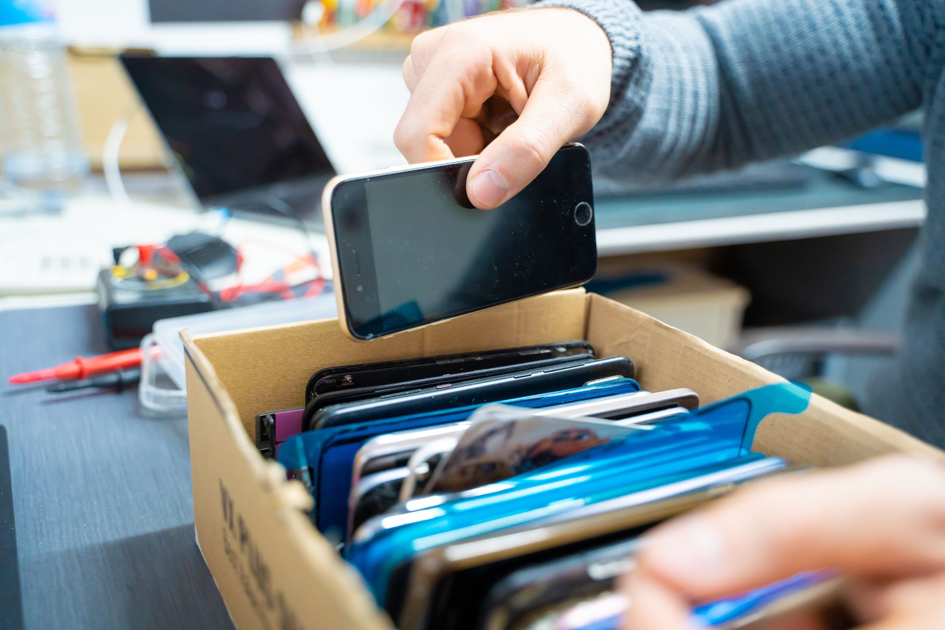 Hand of a man keeping a mobile phone in a box full of broken mobiles